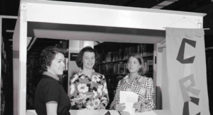 Two Friends of the Library standing  in Circus booth talking with a library patron about the event.