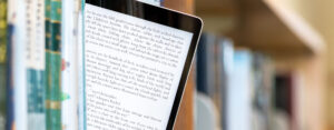 An eBook on an iPad sticking out around other books on a bookshelf
